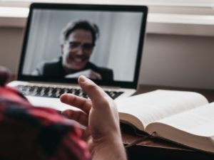 A student on a video call with a professor and a textbook.